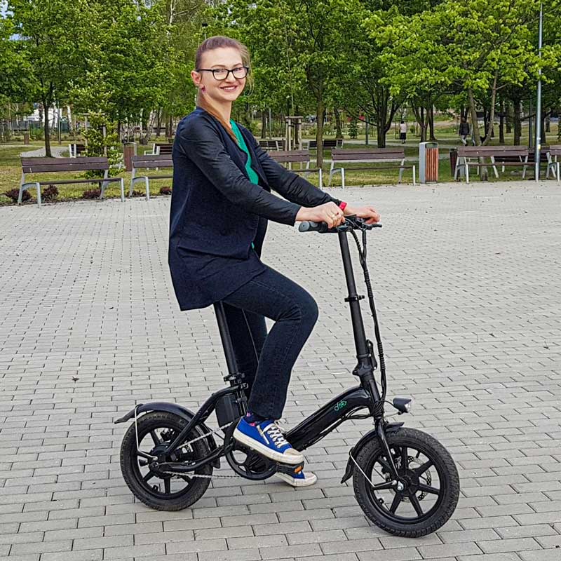 A girl parks her Fiido D3 Pro on a brick paved ground in a park and sits on the bike